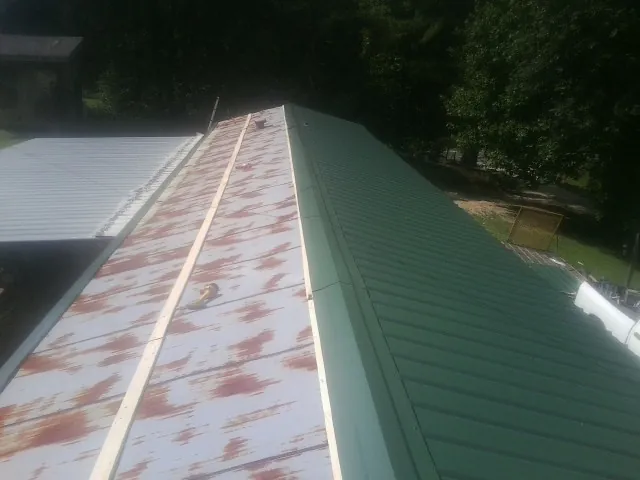 Old rusted panels beside newly installed green metal roofing — Wind Damage Roof Repair by Roofing Brothers in Huntsville